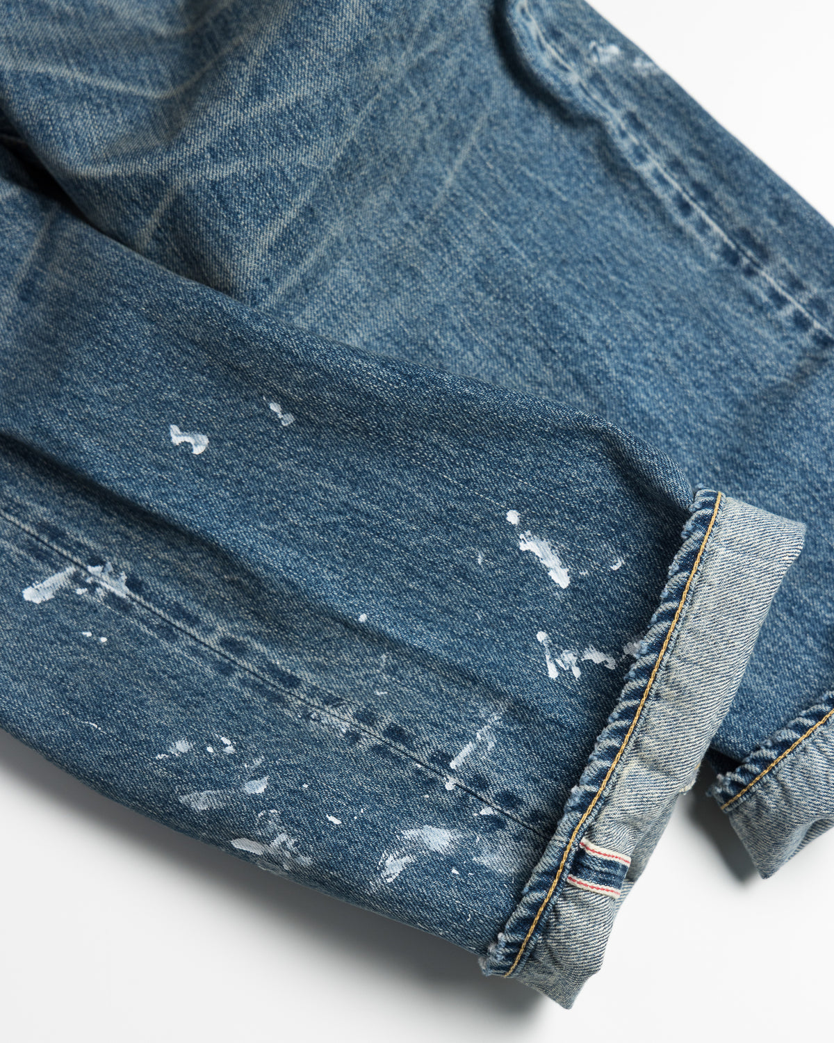 Close-up of a blue denim fabric with white paint splashes on a white background
