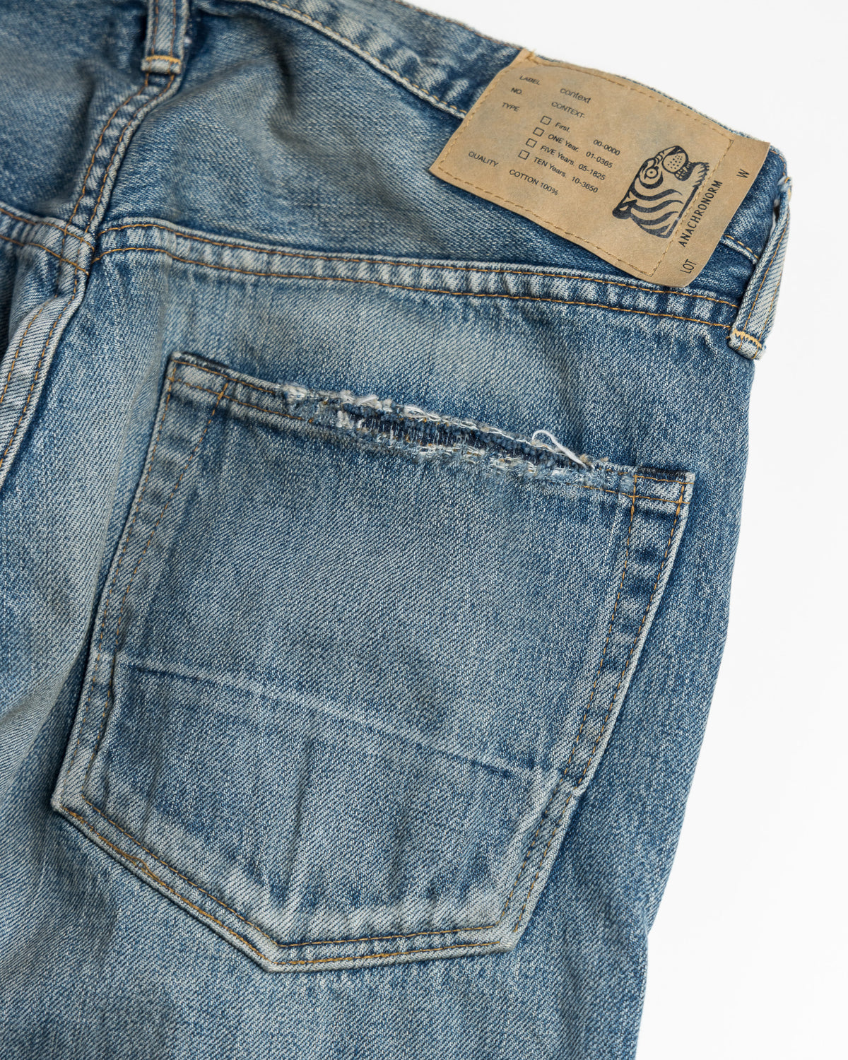 Close-up of blue denim jeans with a Soulgoods brand tiger head logo label on a white background