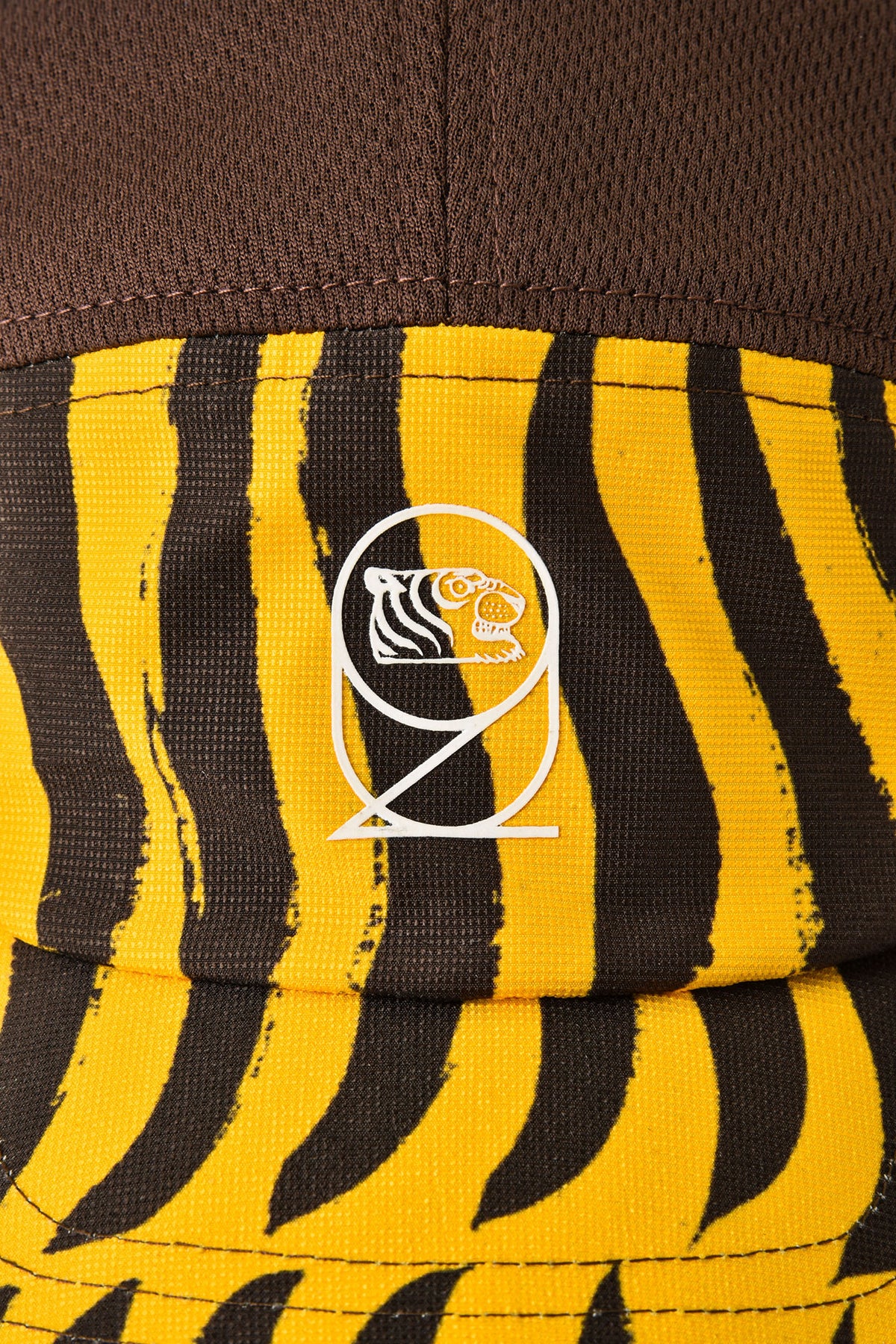 Close-up of a cap featuring a brown crown and a yellow and black tiger-stripe patterned brim, with a white Dosnovent x SOULGOODS tiger logo centered on the front.