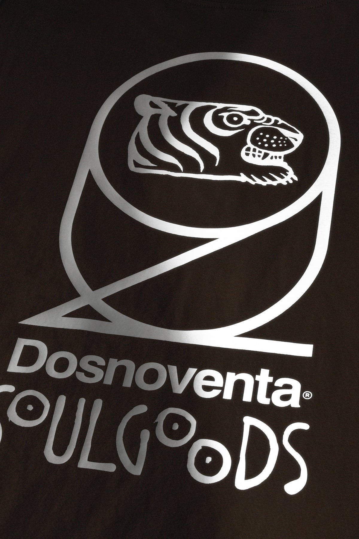 Close-up of a dark brown or black garment featuring a large white graphic print. The design shows a stylized tiger head inside a circular outline above the text 'Dosnoventa soulgoods'.
