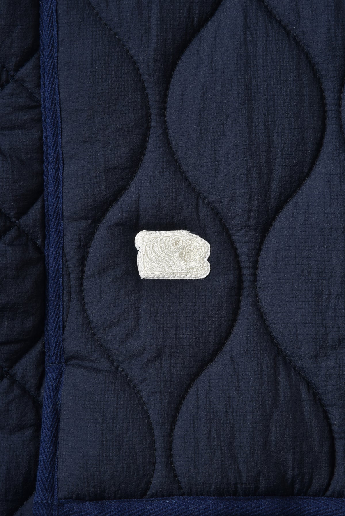 Close-up of a dark blue quilted fabric with a white soulgoods tiger head embroidered design.