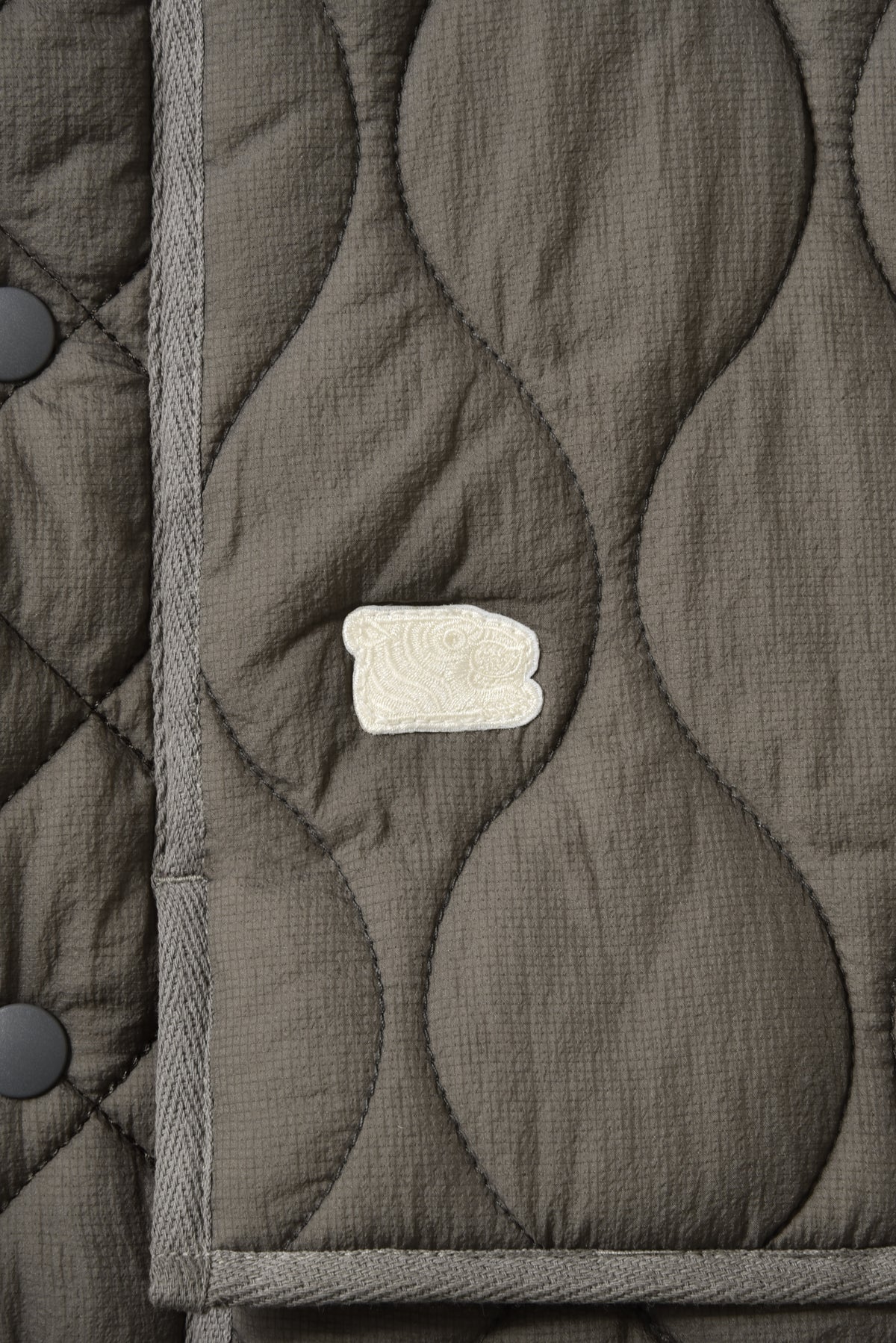 Close-up of a quilted jacket with a Soulgoods tiger head logo on a dark gray background