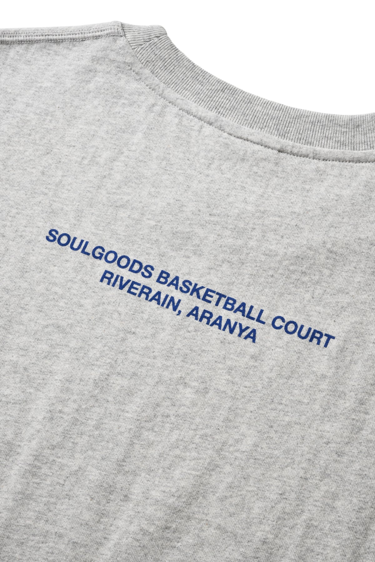 Close-up of a light heather gray t-shirt showing the back collar and blue printed text that reads 'SOULGOODS BASKETBALL COURT RIVERAIN, ARANYA'.