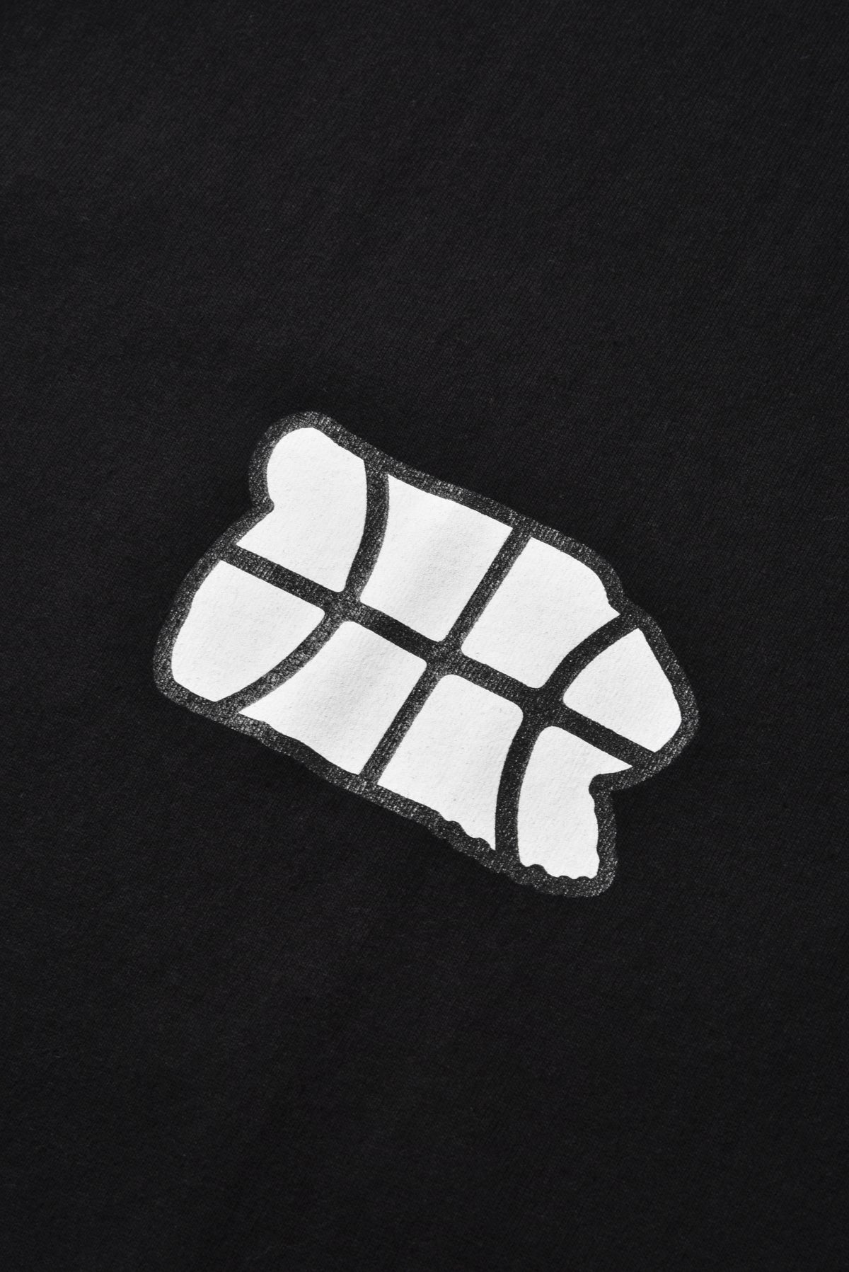 A close-up of a black garment featuring a white embroidered patch with a geometric, segmented design and a dark outline.