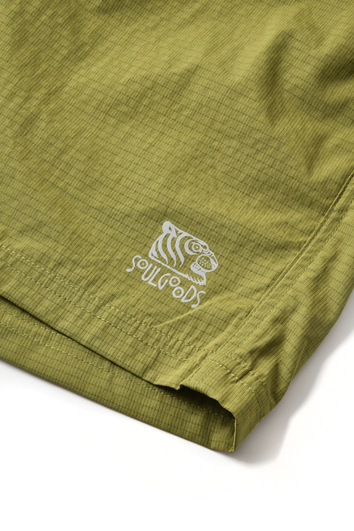 Close-up of olive green textured shorts with a white embroidered tiger head logo and the word 'SOULGOODS' on the lower left leg, shown against a white background.