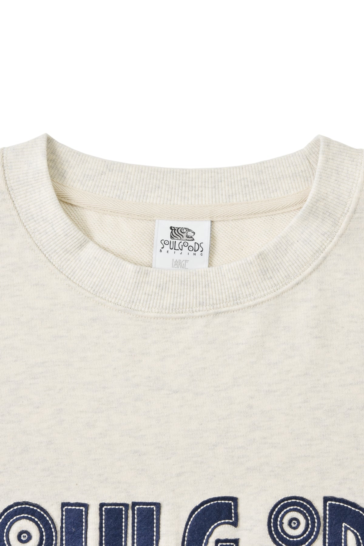 Close-up of a oatmeal-colored sweatshirt with a soulgoods brand label on the collar.
