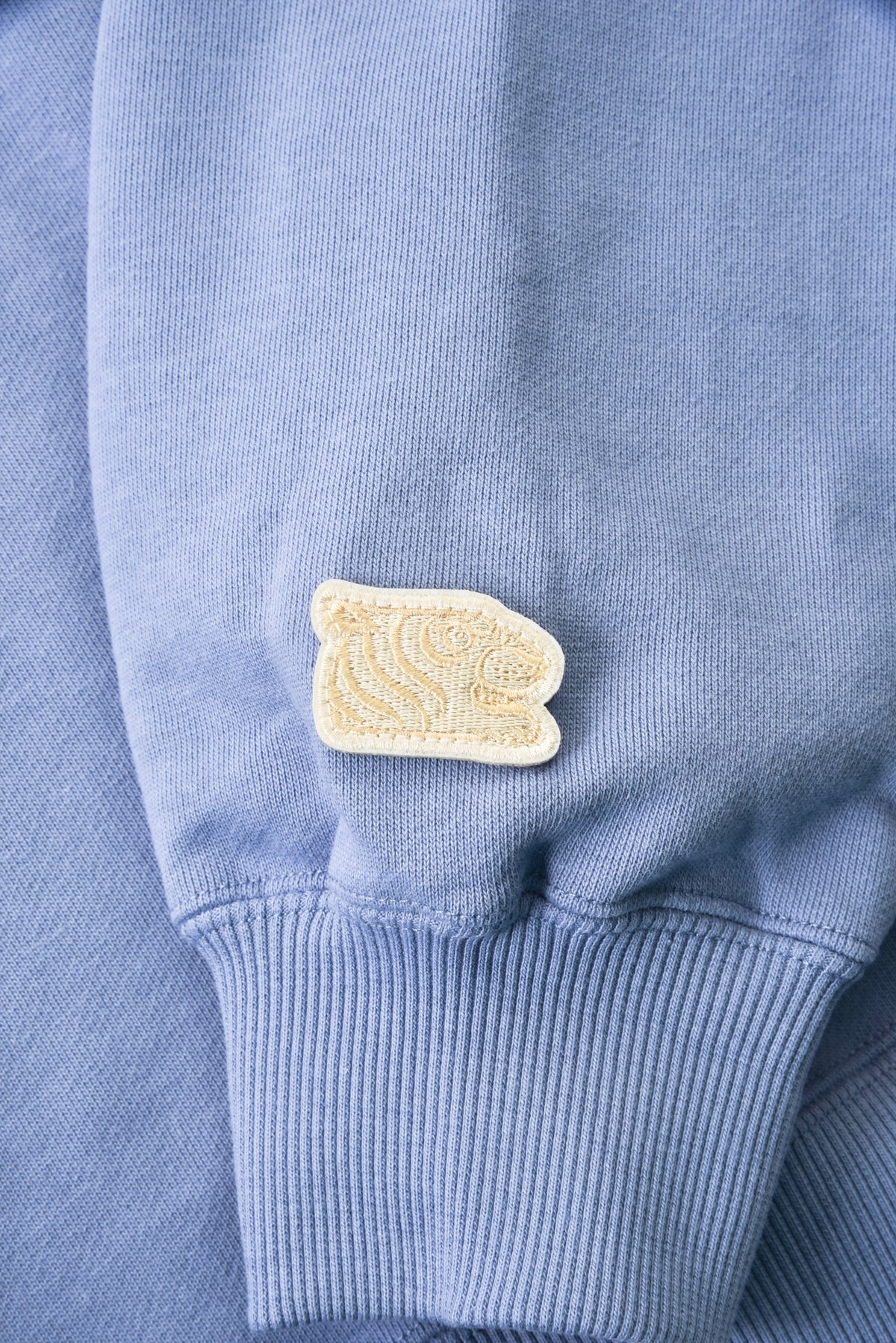 Close-up of a blue sweater with a beige patch on the sleeve.