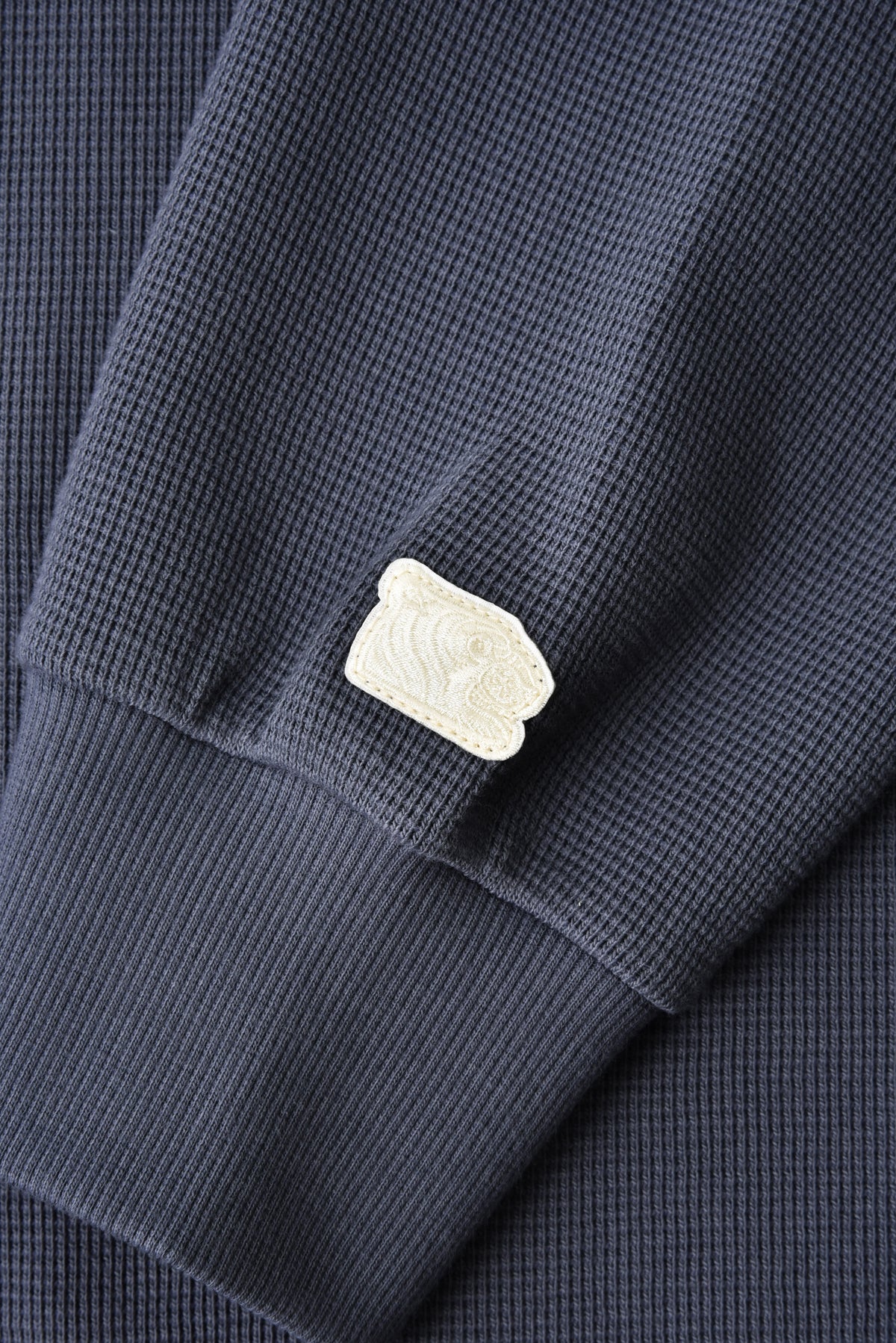 Close-up of a navy blue textured shirt with a white soulgoods tiger head on a matching fabric background