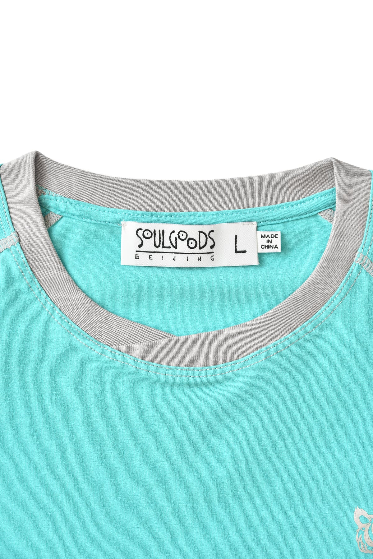 Close-up of a turquoise shirt with gray trim and a SOULGOODS label on a white background