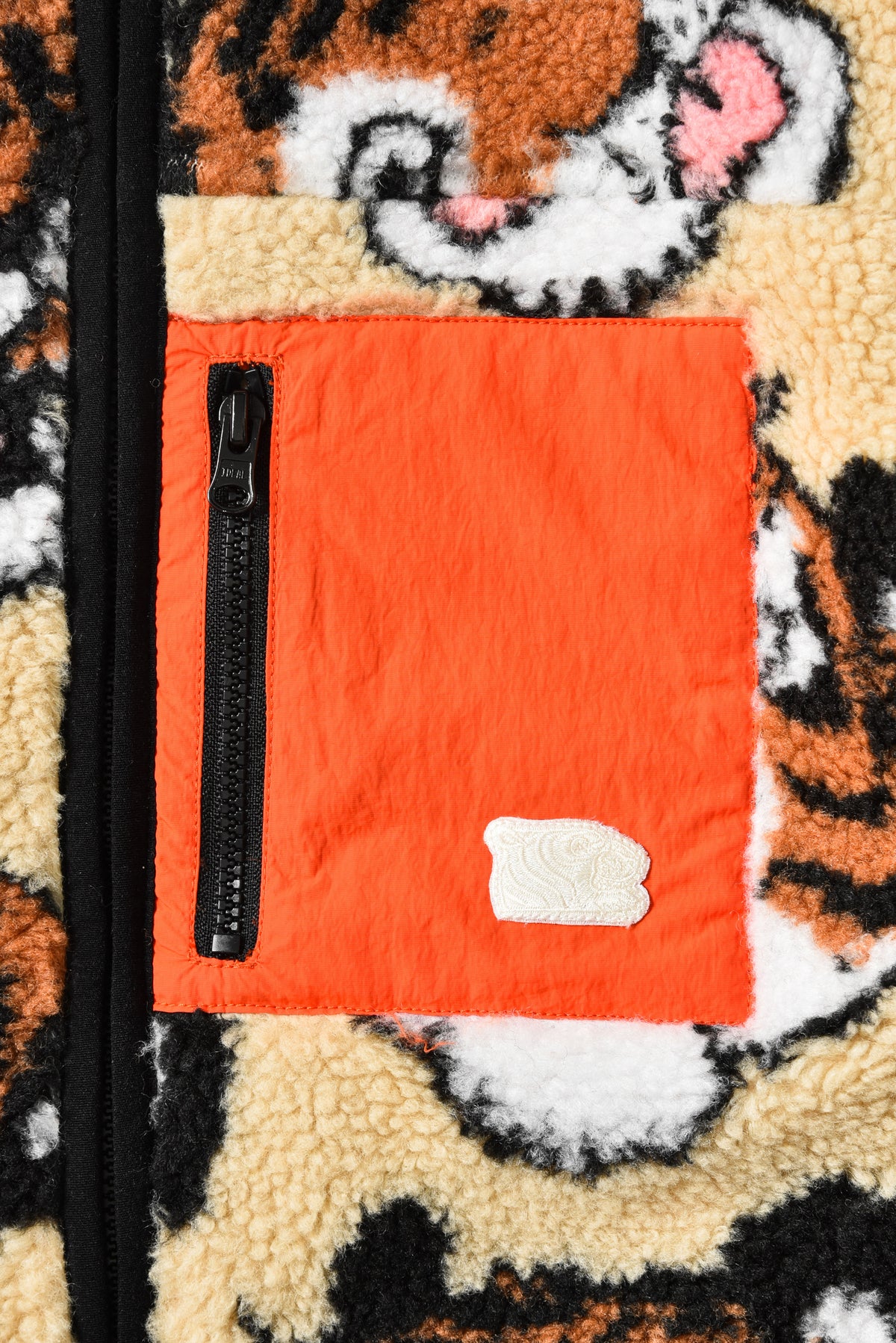 Close-up of a textured fabric with a tiger pattern and an orange pocket with a zipper.