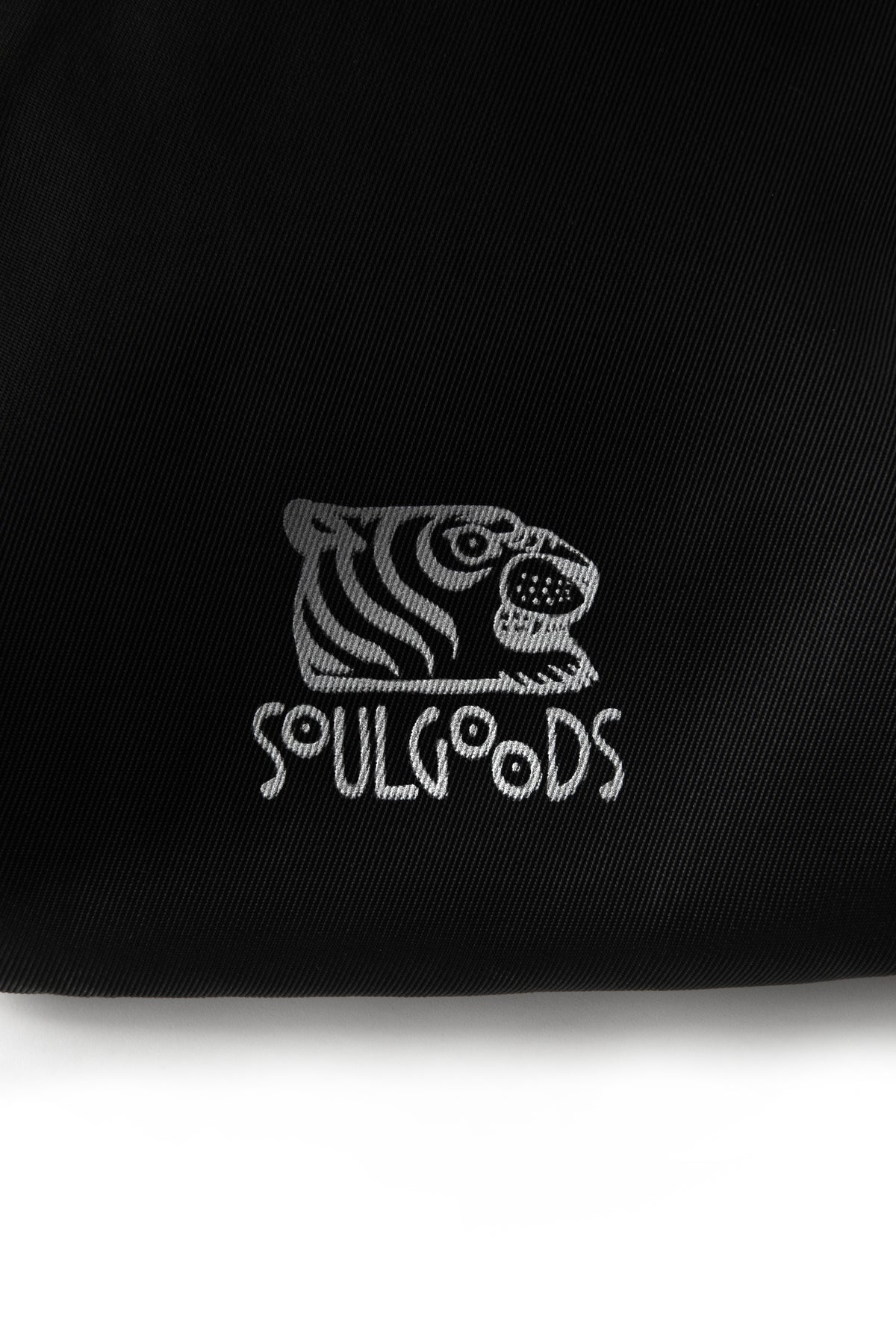 Close-up of a black fabric item featuring a white embroidered tiger head logo and the word 'SOULGOODS' below it, against a white background.