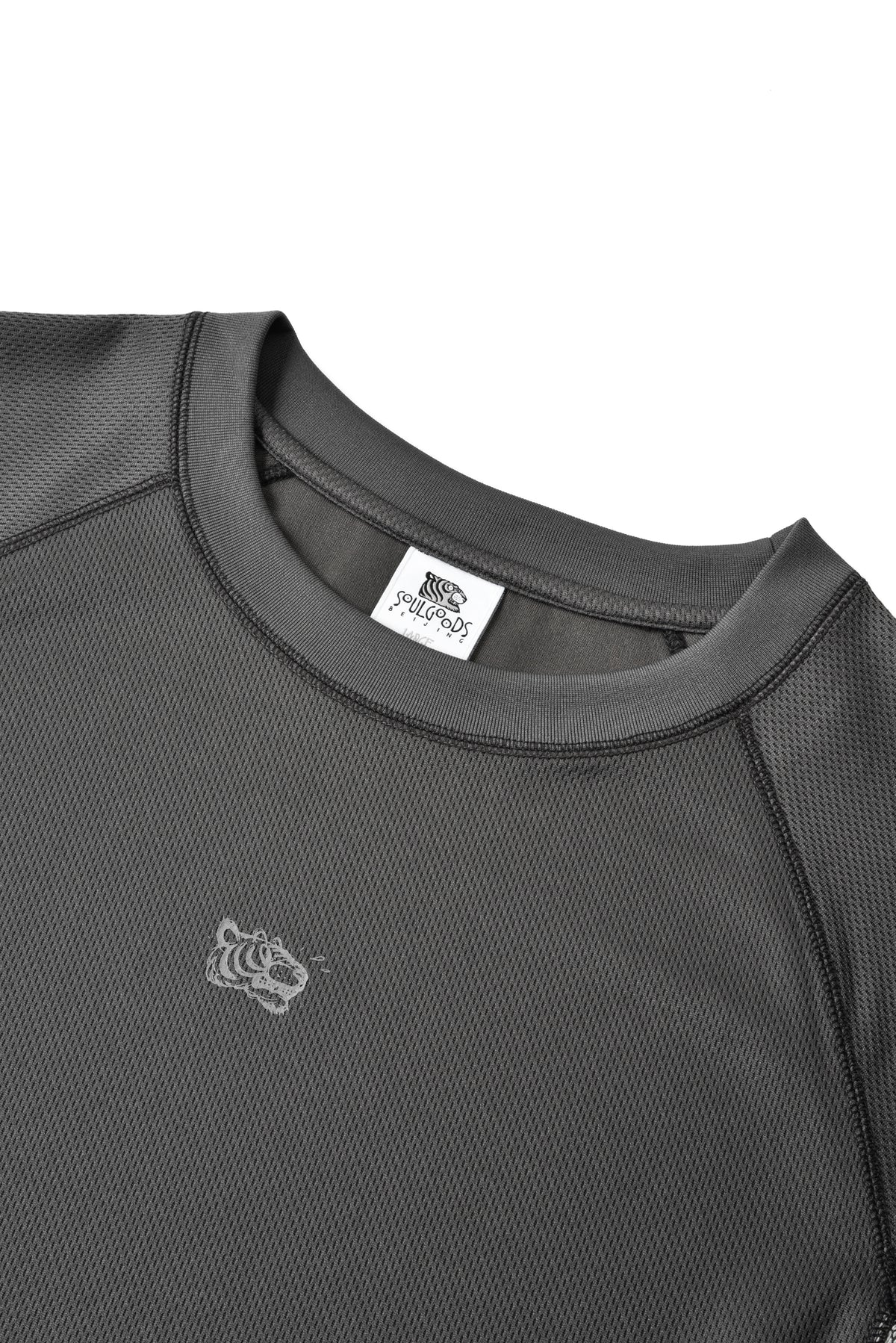 Close-up of a dark gray athletic crewneck shirt with a textured mesh fabric, a white neck label, and a small white tiger logo on the chest.