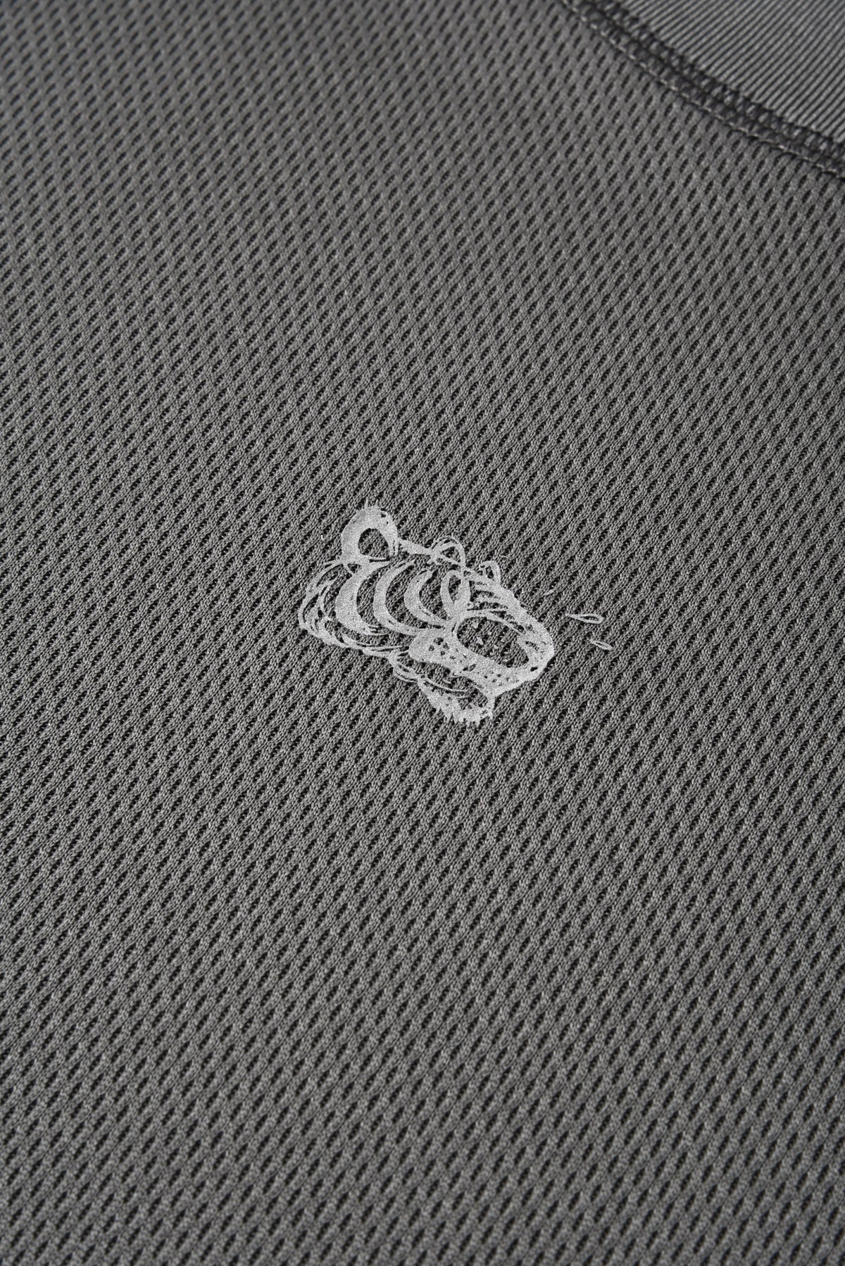 Close-up of a dark gray textured knit fabric with a small white embroidered tiger head logo in the center.