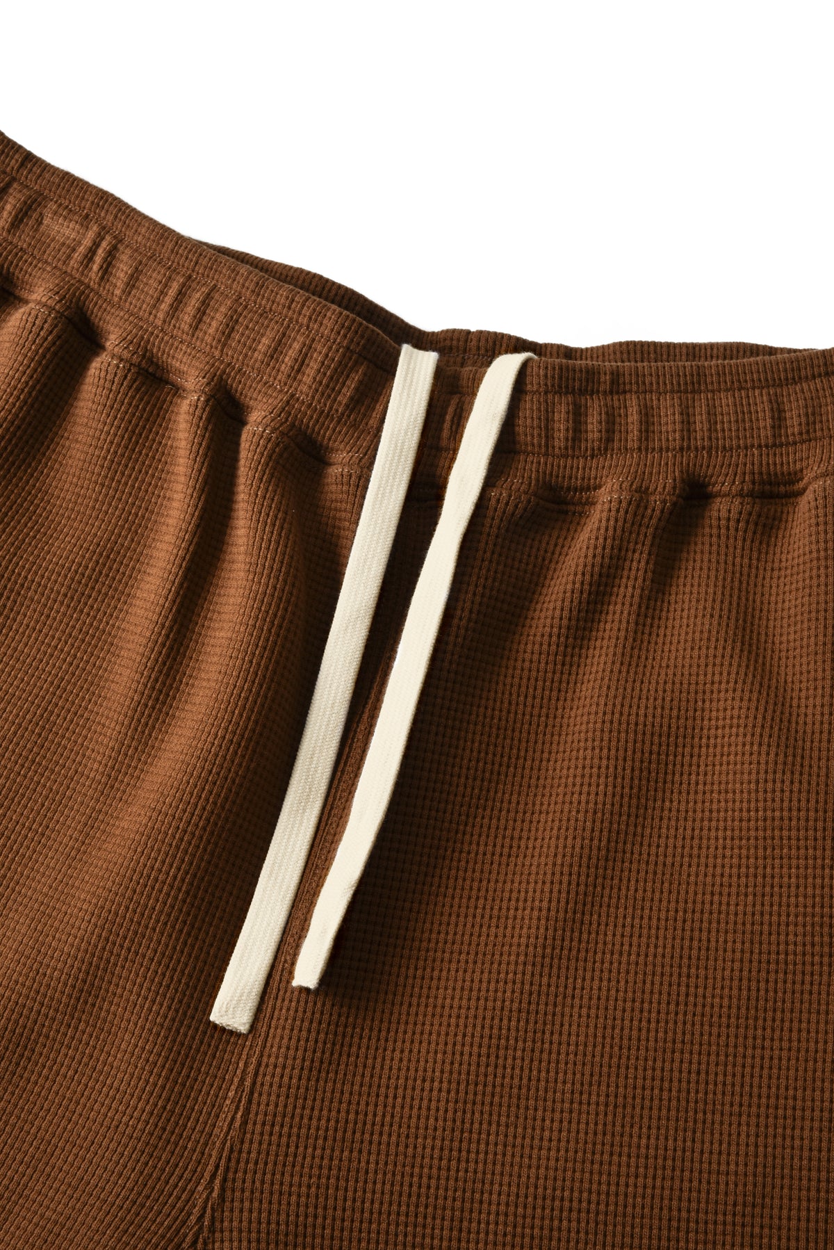 Close-up of brown textured shorts with a white drawstring on a white background.