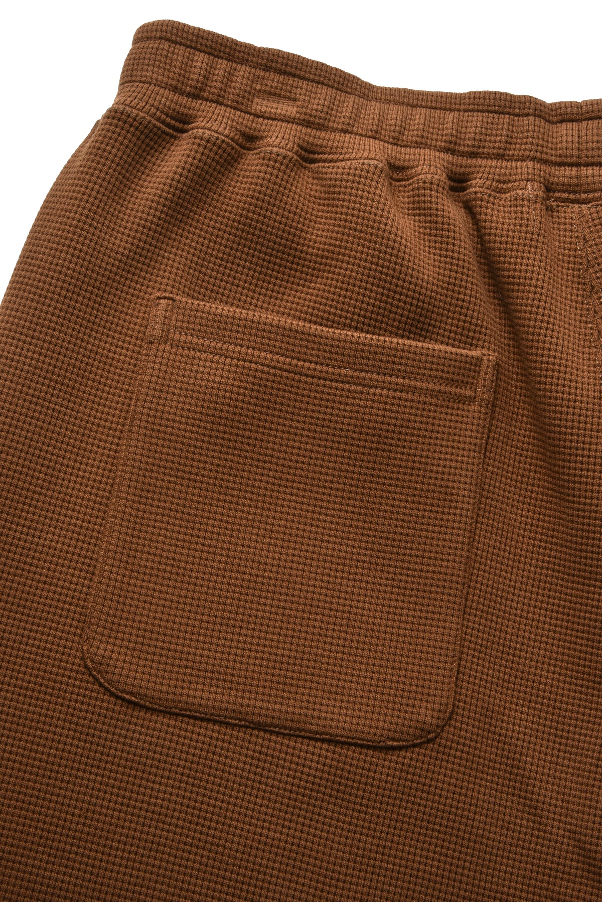 Close-up of brown textured fabric with an elastic waistband and a single front patch pocket.
