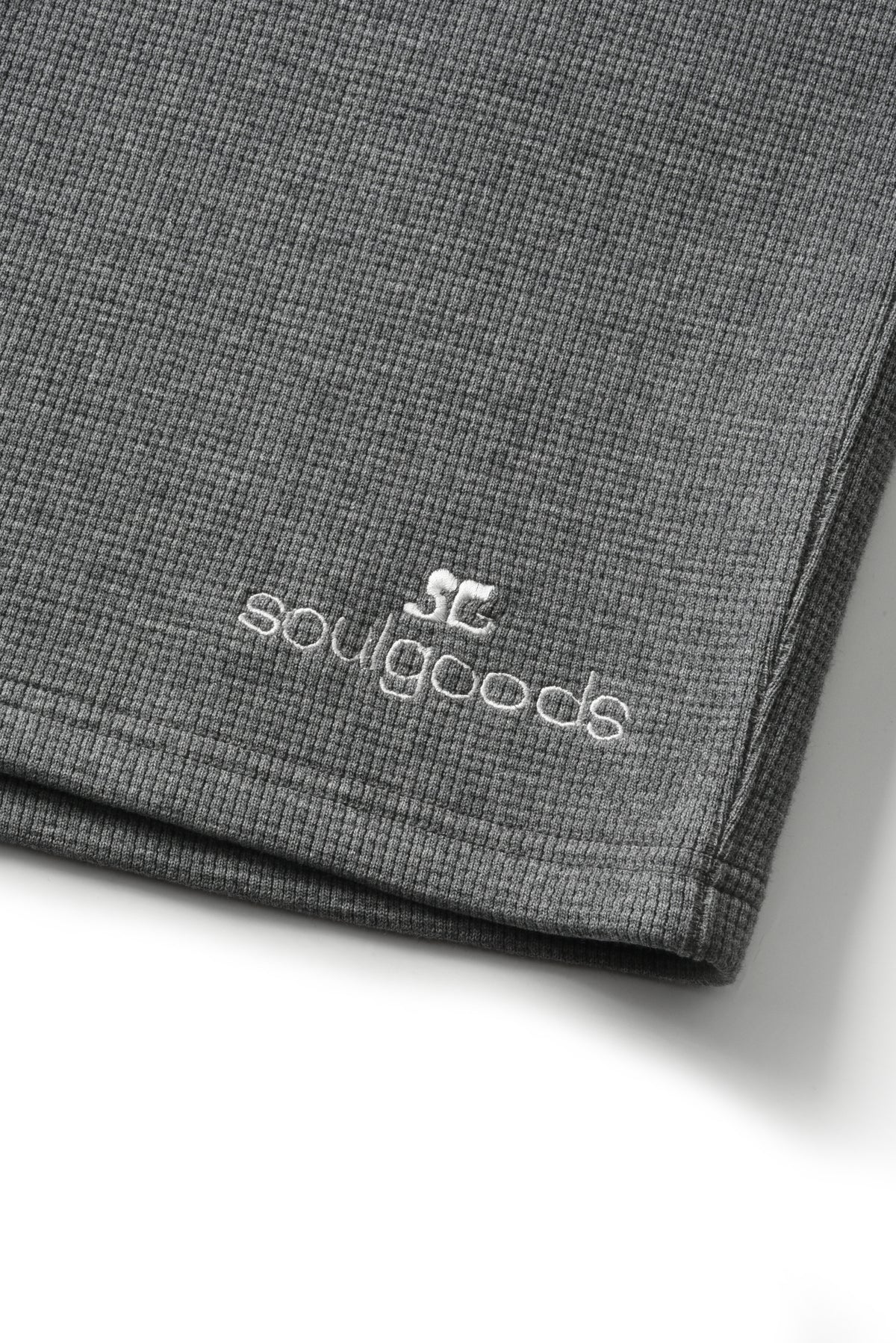 Close-up of a folded dark gray ribbed fabric item, likely a sweatshirt or sweater, with white embroidered 'soulgoods' branding and a small SC logo on the lower left.