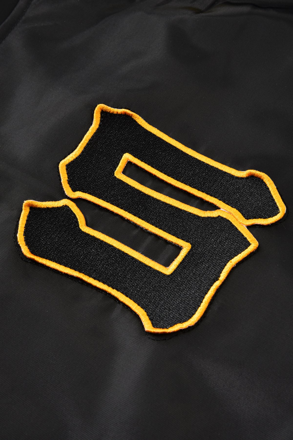 Black jacket with a yellow "S" letter embroidered logo on a black background
