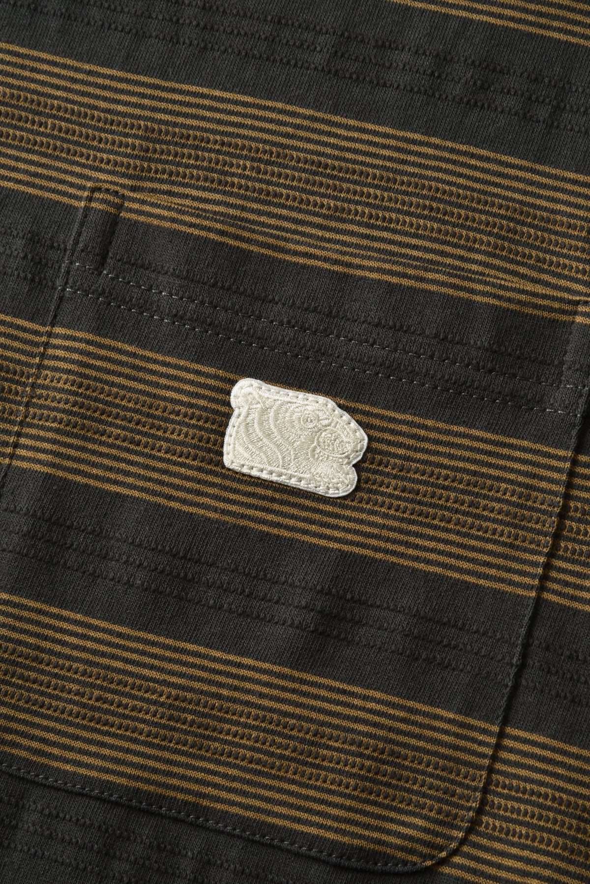 Close-up of a striped fabric pocket with a small white embroidered patch on a black and brown striped garment.