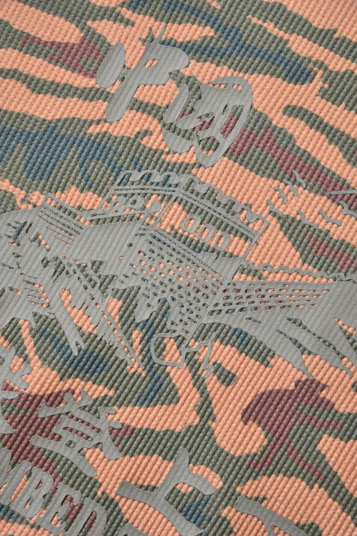 Camouflage-patterned fabric with embroidered text on a textured background