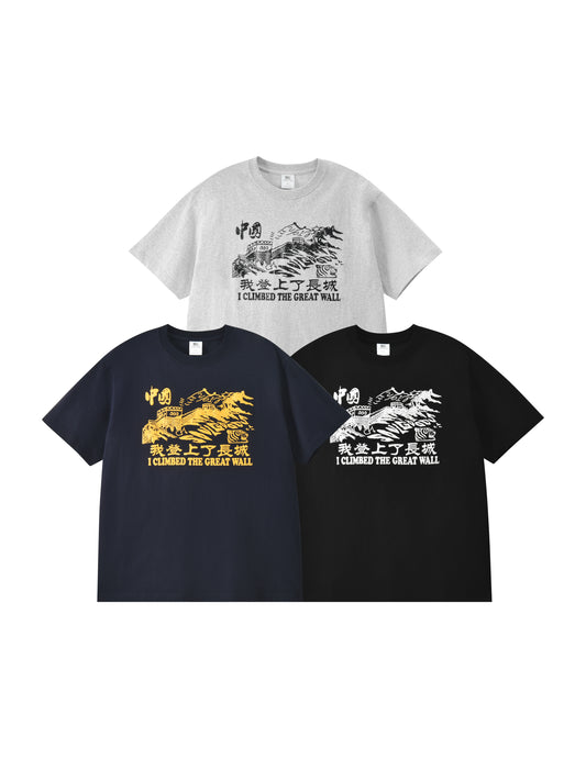 Three graphic T-shirts shown on a plain white background: one light gray shirt at the top with a black the great wall print and text, one dark navy shirt at lower left with a yellow print, and one black shirt at lower right with a white print.