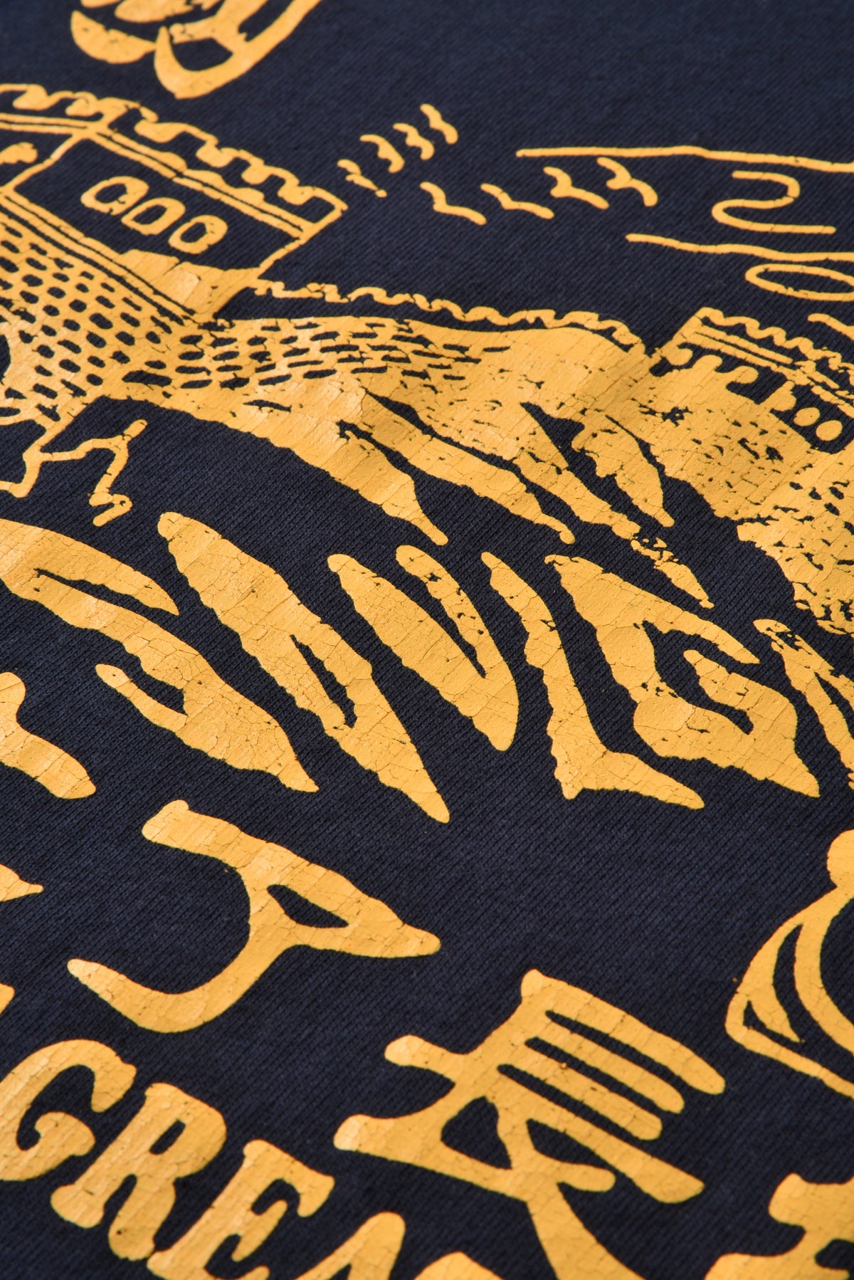 Close-up of a navy blue fabric with a distressed gold graphic print featuring stylized text and illustrated elements.