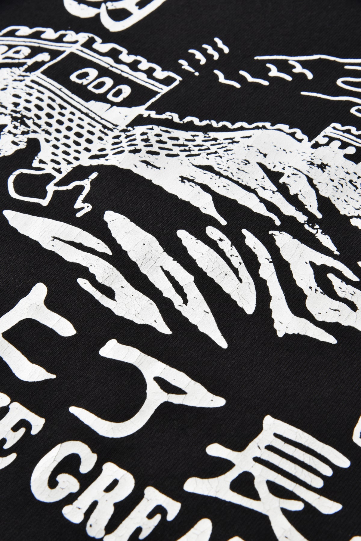 Close-up of a black graphic t-shirt featuring a distressed white print of a castle, waves, and stylized text.