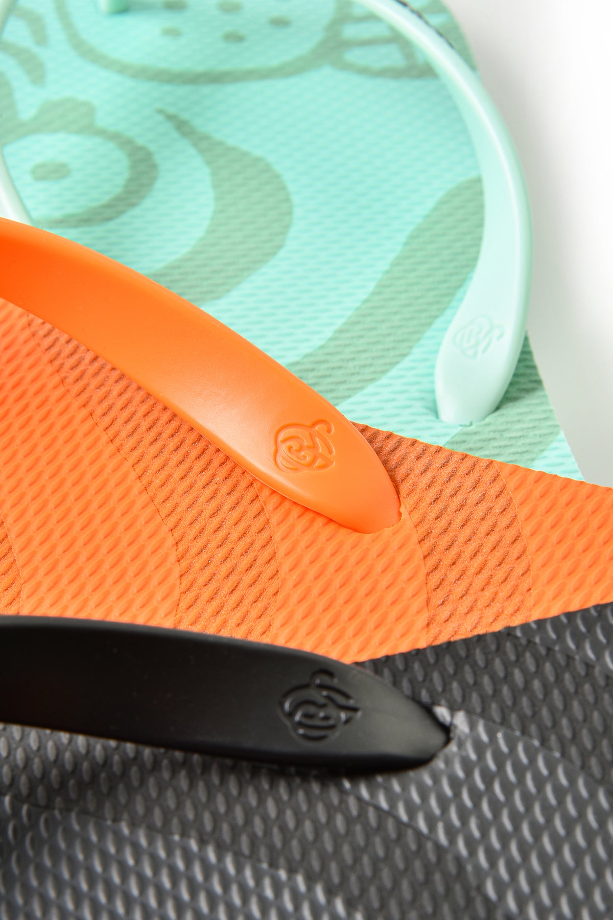 Close-up of a flip-flop sandal showing an orange strap, a mint green textured footbed with a cartoon pattern