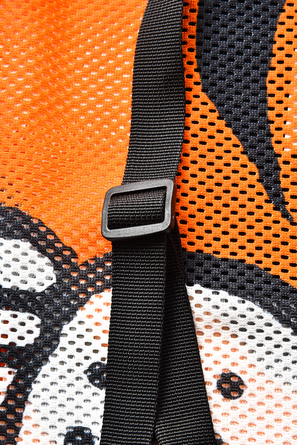 Close-up of a black mesh fabric with a bold orange, black, and white graphic pattern and a black adjustable strap with a plastic buckle.