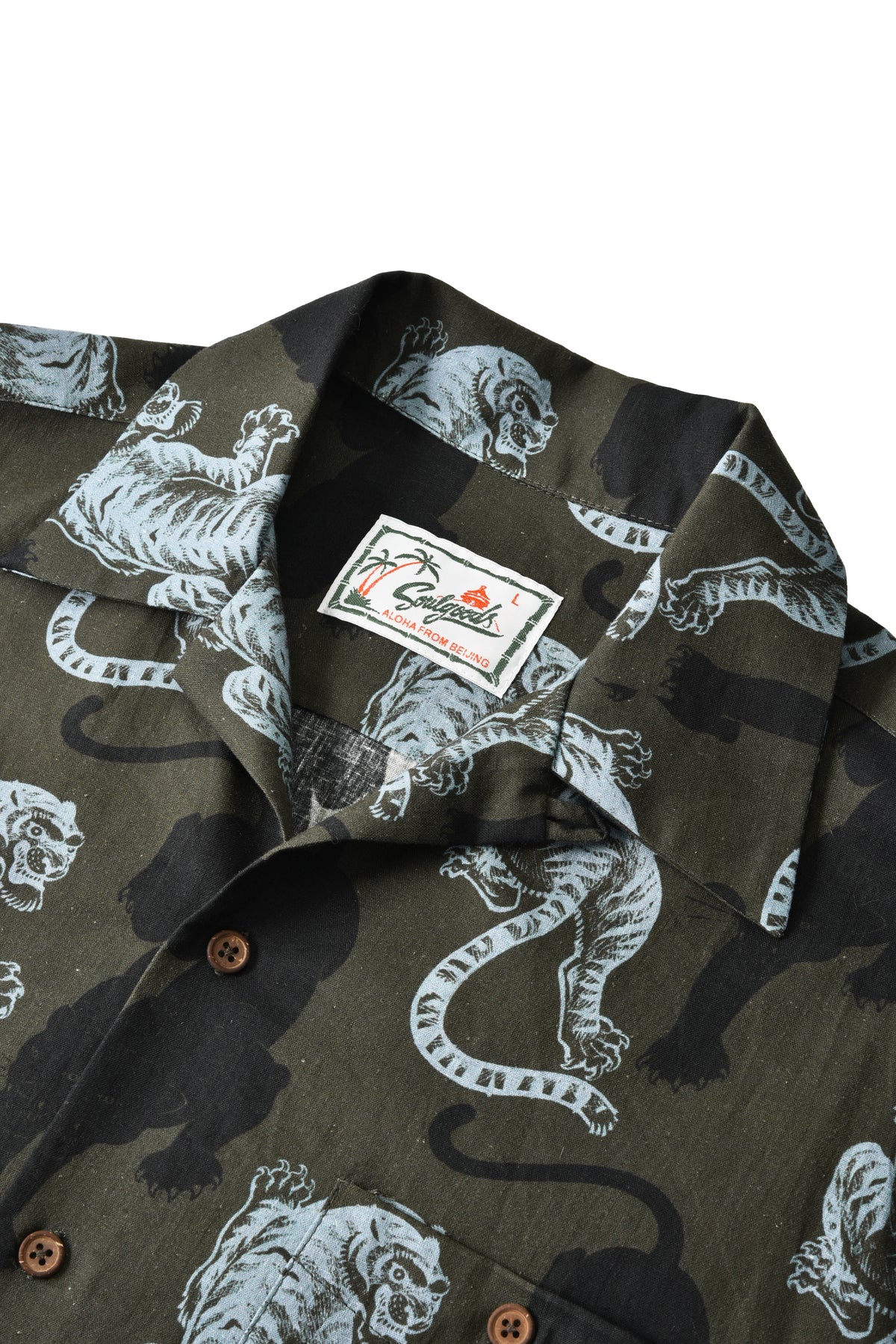 Close-up of a short-sleeve button-up shirt with an all-over tiger print in olive green, black, and white, featuring a visible 'soulgoods' brand label on the collar.