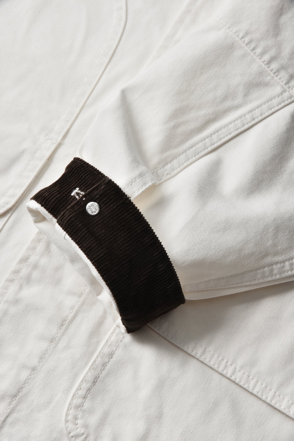 Close-up of a white jacket with a black patch featuring a button on a light gray background