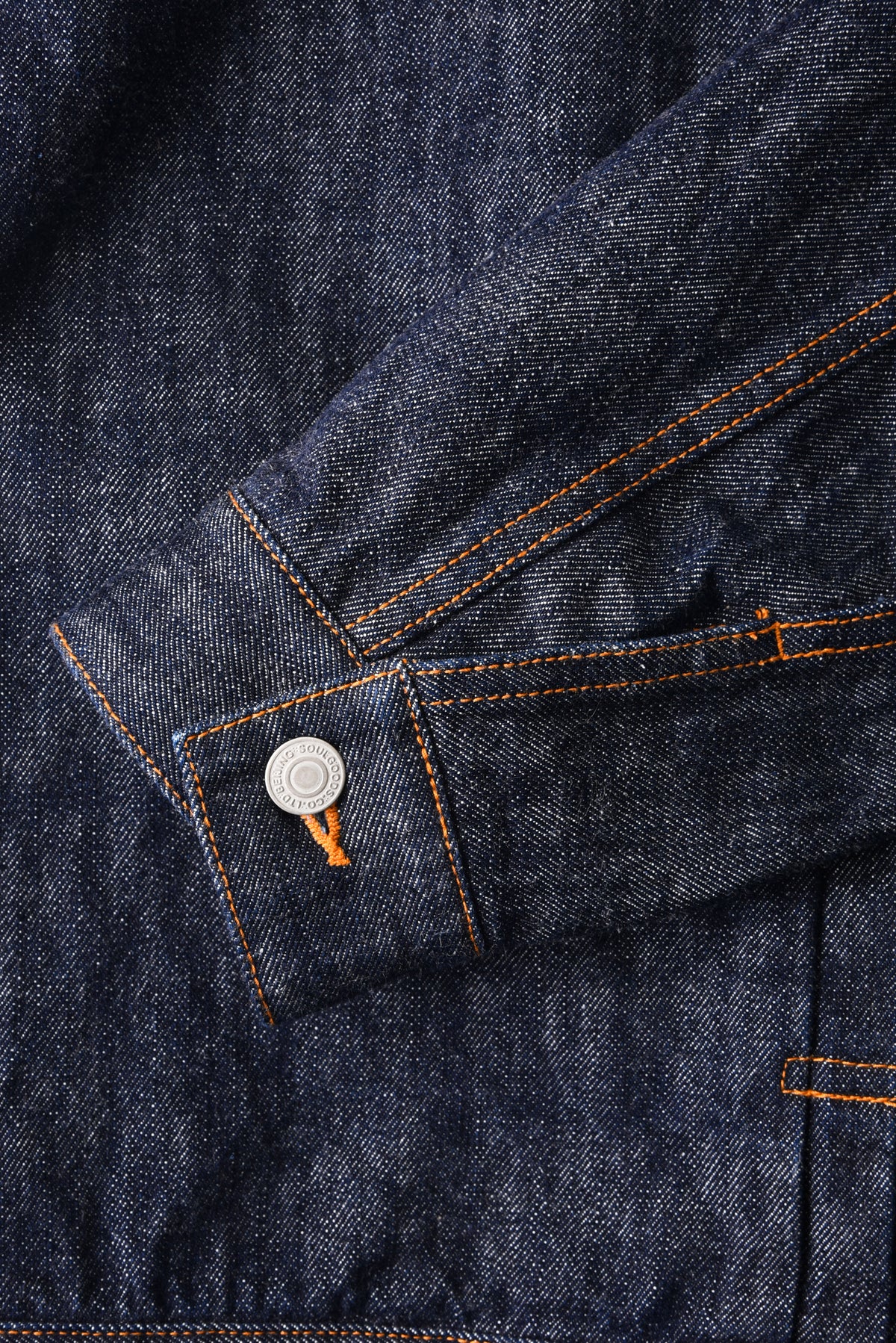 Close-up of a blue denim jacket with orange stitching and a button.