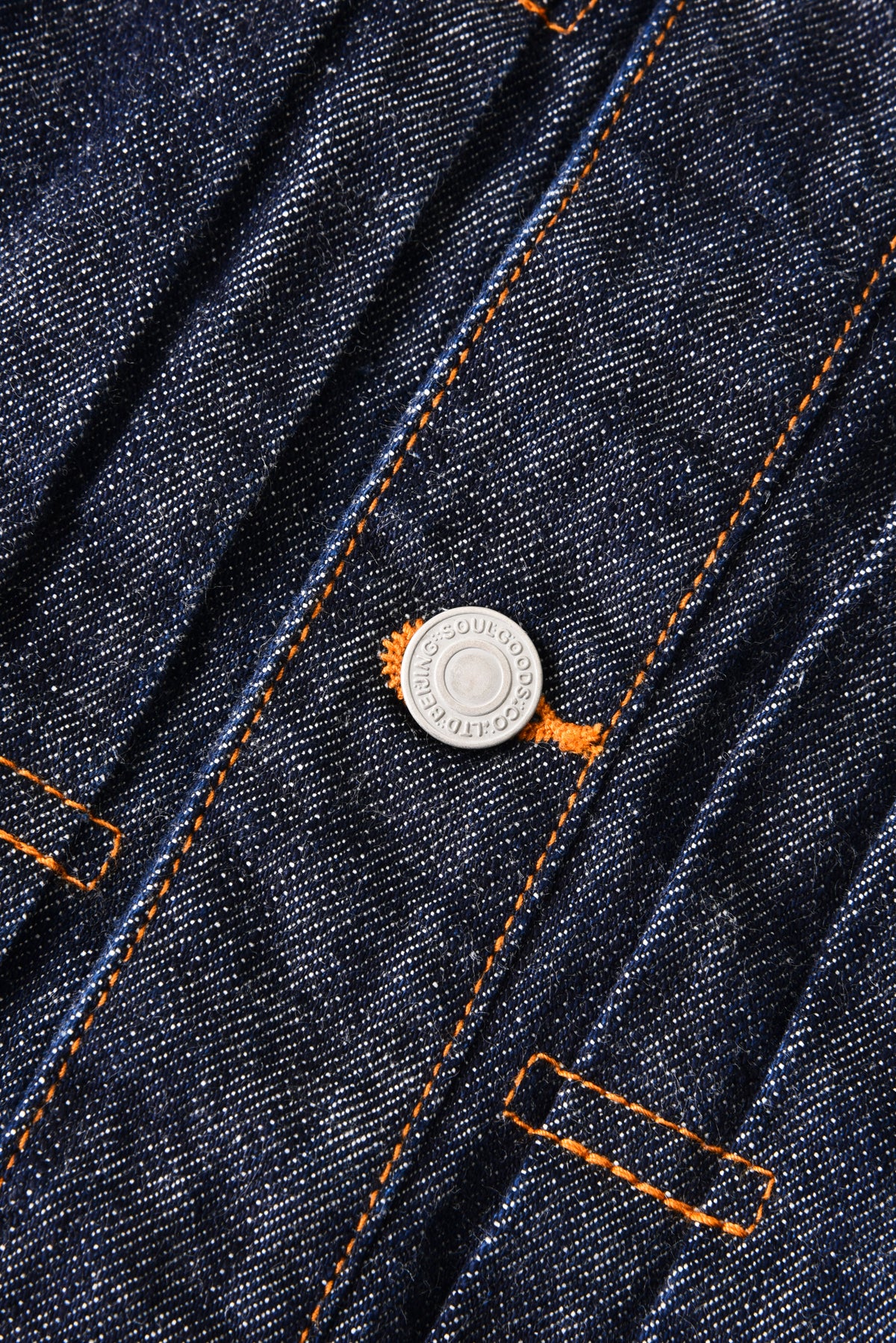 Close-up of a blue denim jacket with orange stitching and a button.