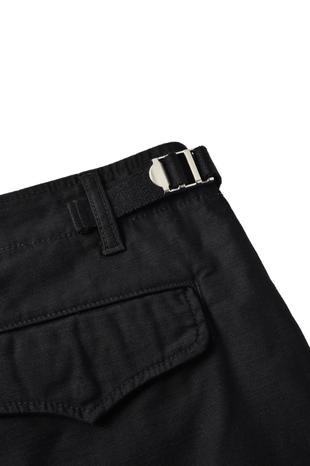 Close-up of black trousers showing the waistband with a silver metal buckle and a side pocket, photographed on a white background.