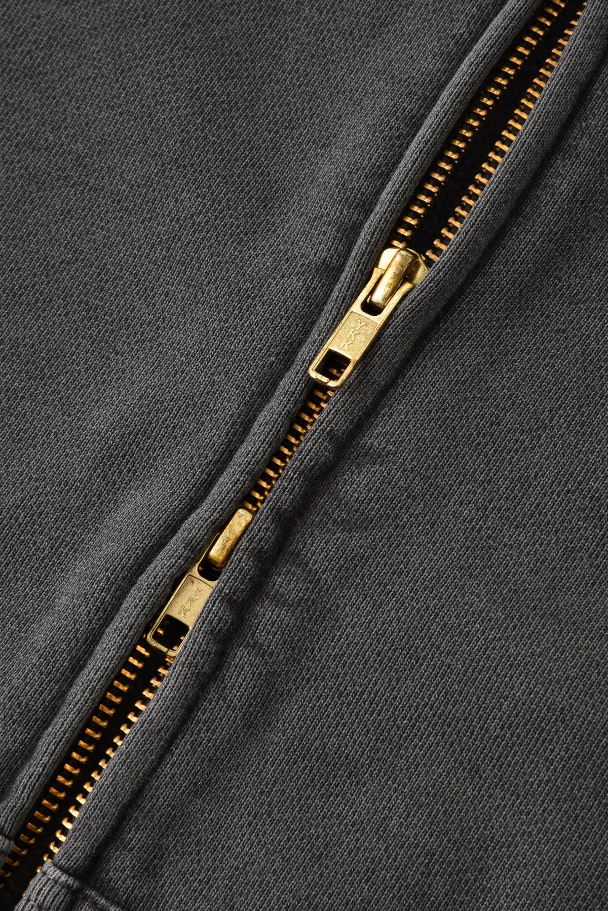 Close-up of a gold zipper on a gray fabric background