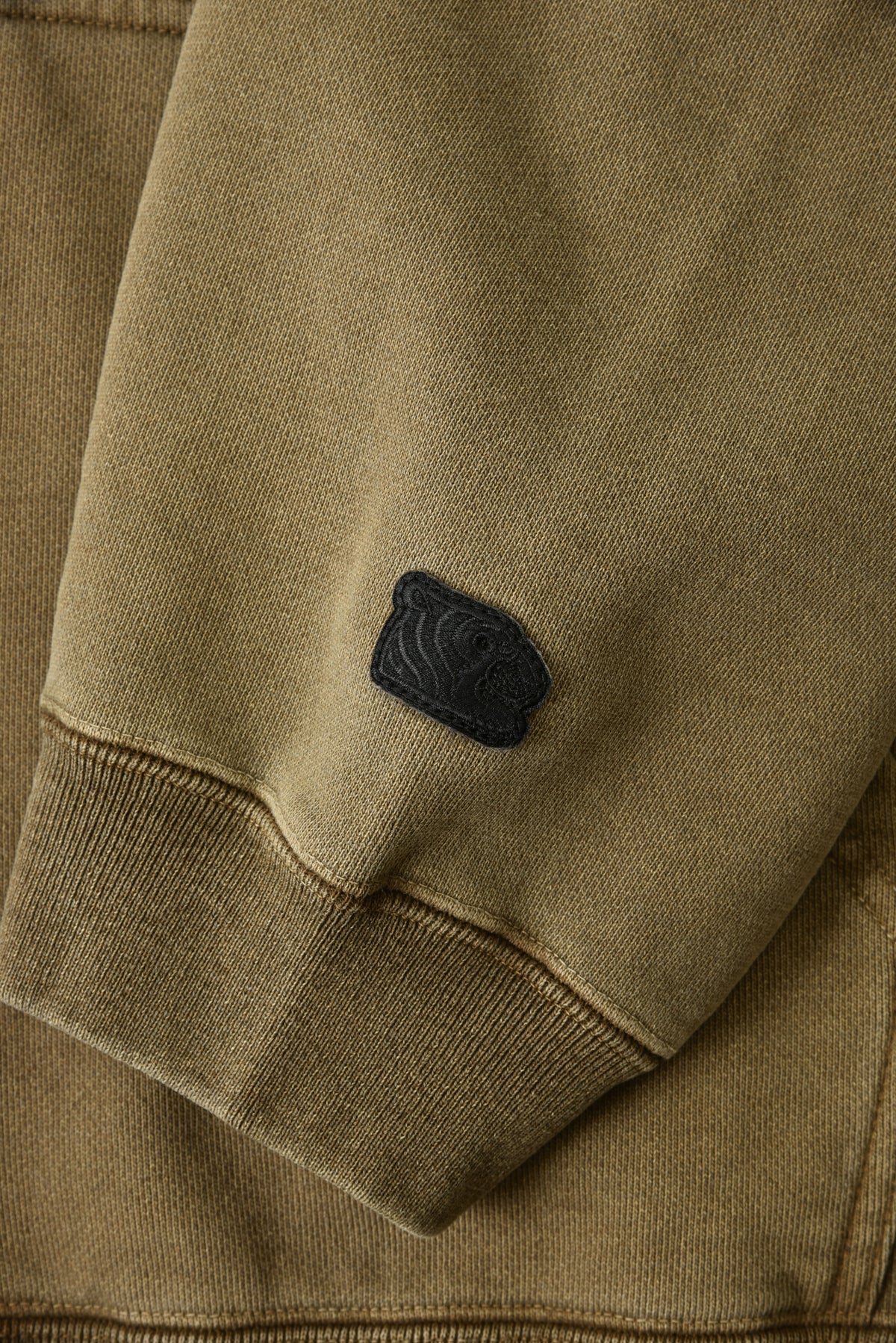 Close-up of a brown jacket with a black logo on the chest.